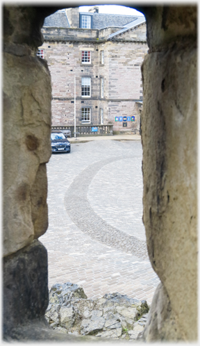 Vertical slit opening in stone wall, building beyond.