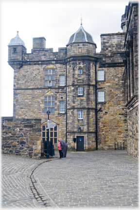 Cobbled area in front of three story building with turrets.