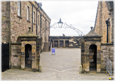 Pair stone Sentry boxes with iron lamp support joining them across a road.