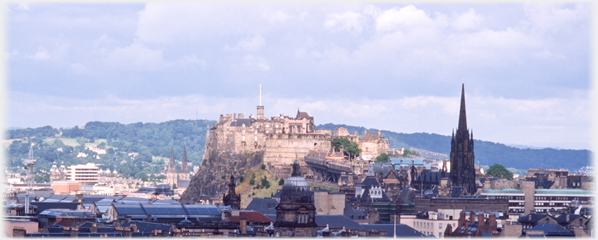 Castle in sunlight contrasting with dark buildings.