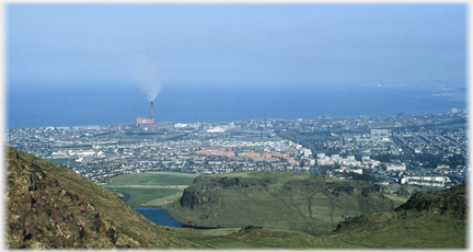 Suburbs with large chimney smoking at coastline.