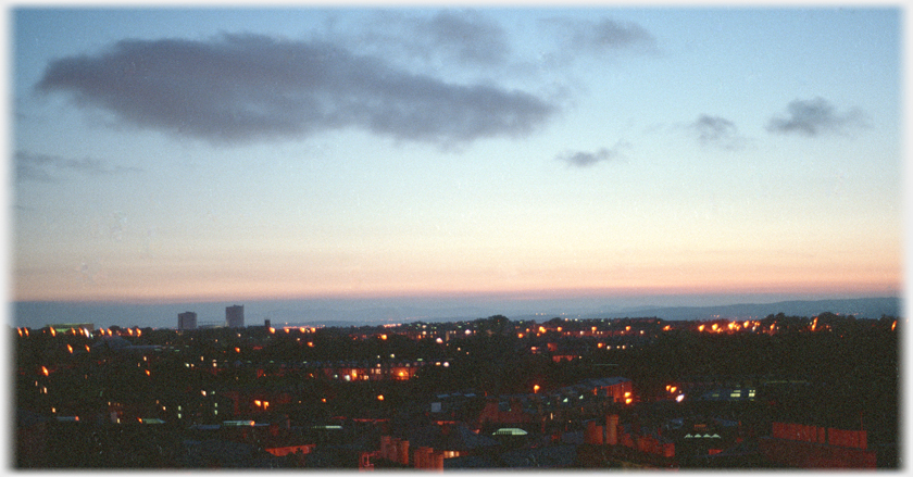 Dark city with points of light and light in sky.