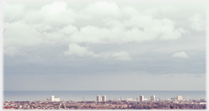 Heavy clouds over sea with narrow band of city at bottom.