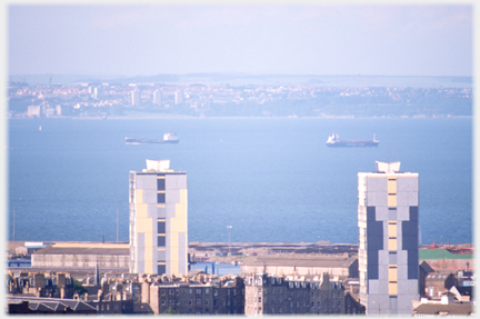 Two tower blocks in foreground with ships and estuary beyond and town on far side.