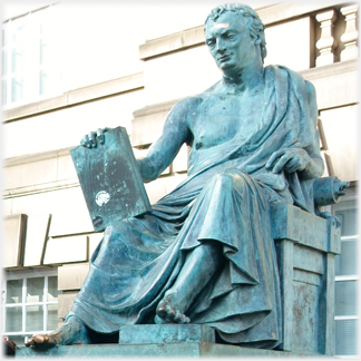 Statue of seated man in toga holding book, bare footed.