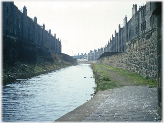 Canal with dark grey tenements on either side.