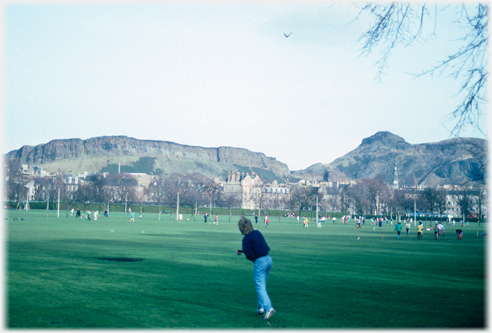 Man throwing boomerang with many figures in far background and hills beyond.