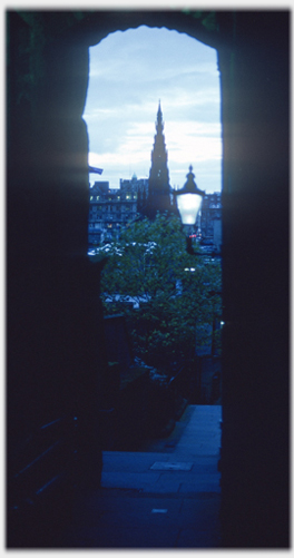 Archway framing monument with street light and other lights showing.