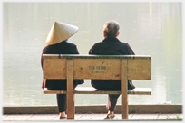 Two people seated beside lake.