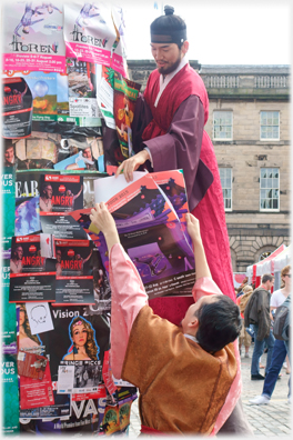 Costumed figures affixing poster to a 'Morris Column'.