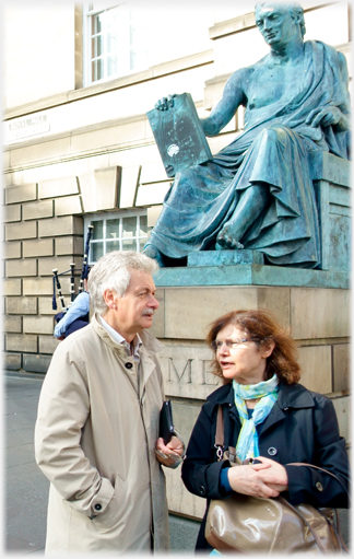 Man and woman talking beneath statue.