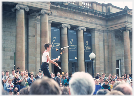 Man on uni-cycle juggling three lit torches.