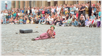 Man lying on cobbles in front of large street audience.