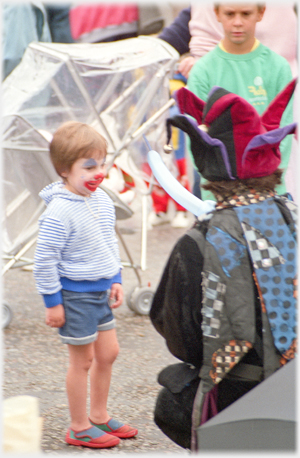 Boy with painted face watching balloons being twisted.