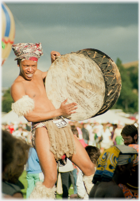 Man in minimal costume holding large drum.