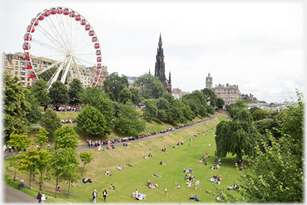 Grass banking with trees above and below, and people spread out into the distance.