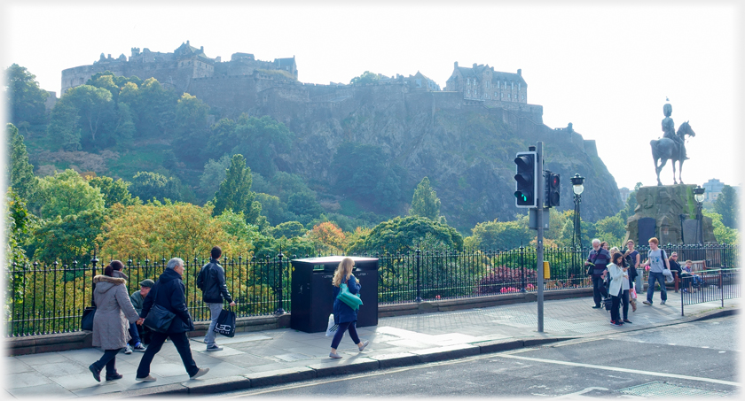 Pavement with people, traffic lights and castle as backdrop.