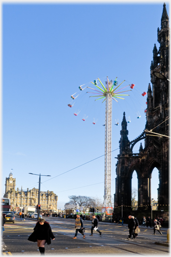 Ornate monument with distant hotel and pillar funfair ride with goldolas flying out at great height.