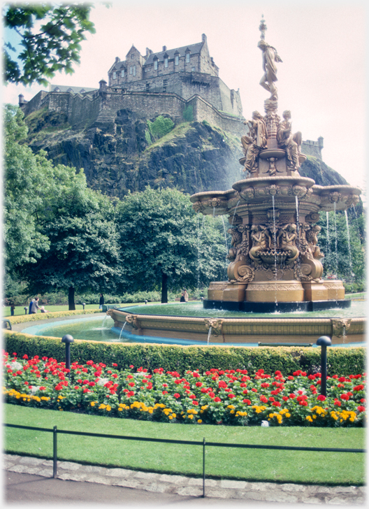 Castle on rocks above gardens with fountain.