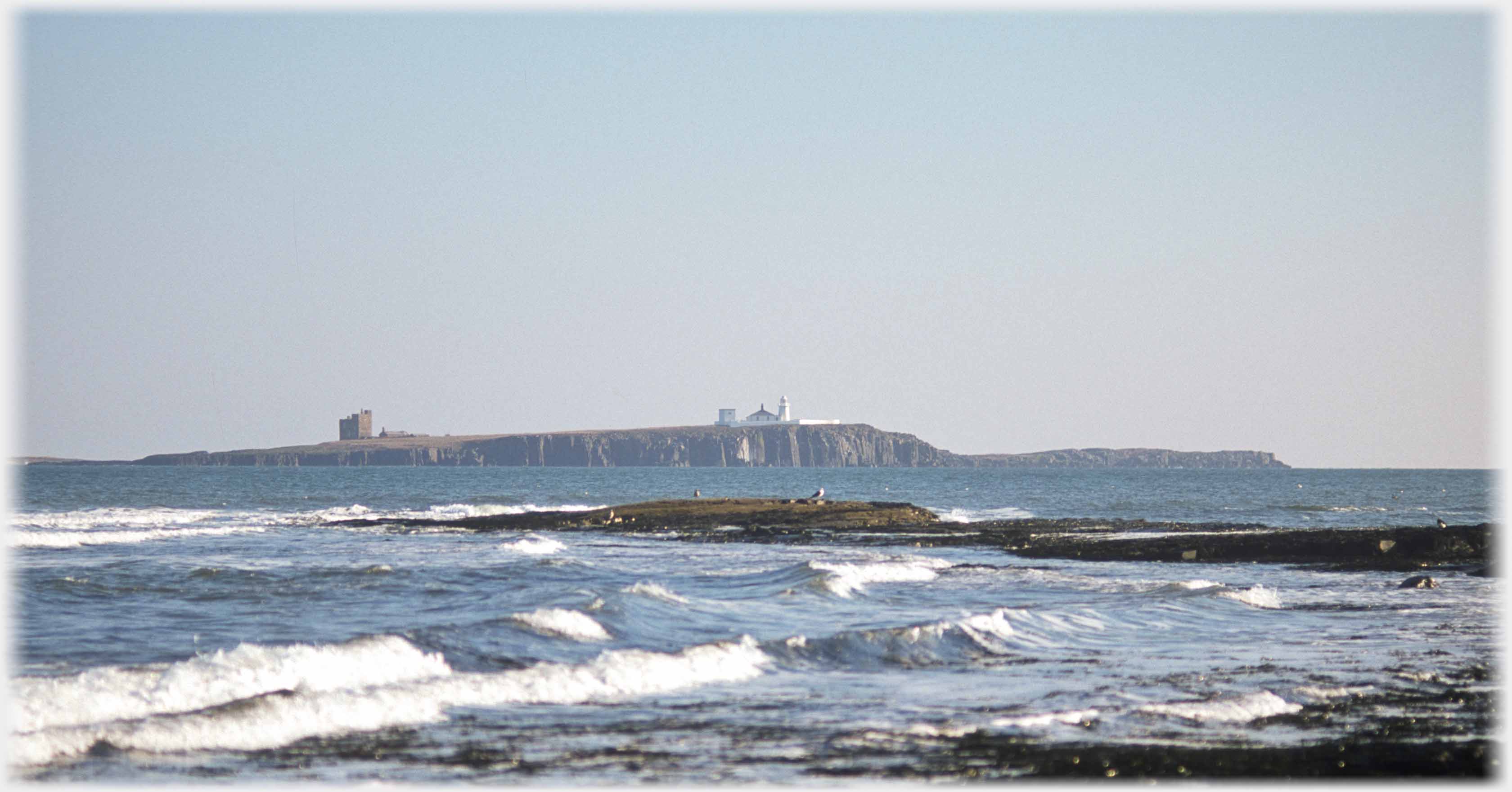 Waves spur of rock and island with lighthouse and tower.