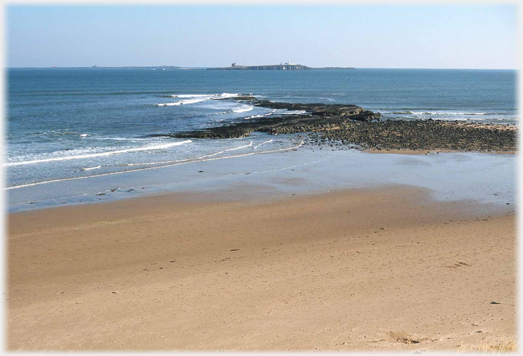 Spur of rock going out from sand pointing at island.