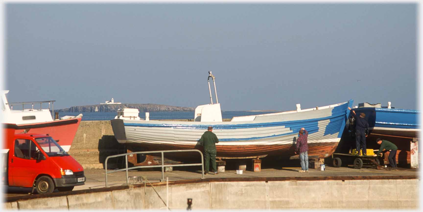 Two men painting the hull of a boat.