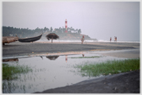 Lighthouse above beech area with boat on sand.