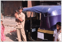 Man holding infant standing by auto.