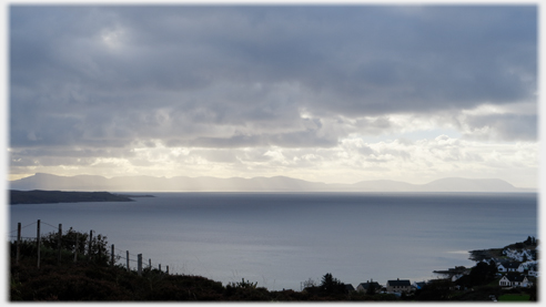 Heavy dark clouds with light breaking through in the distance over outline of hills.