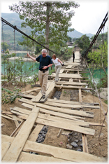 Two people crossing perilous looking suspension bridge.