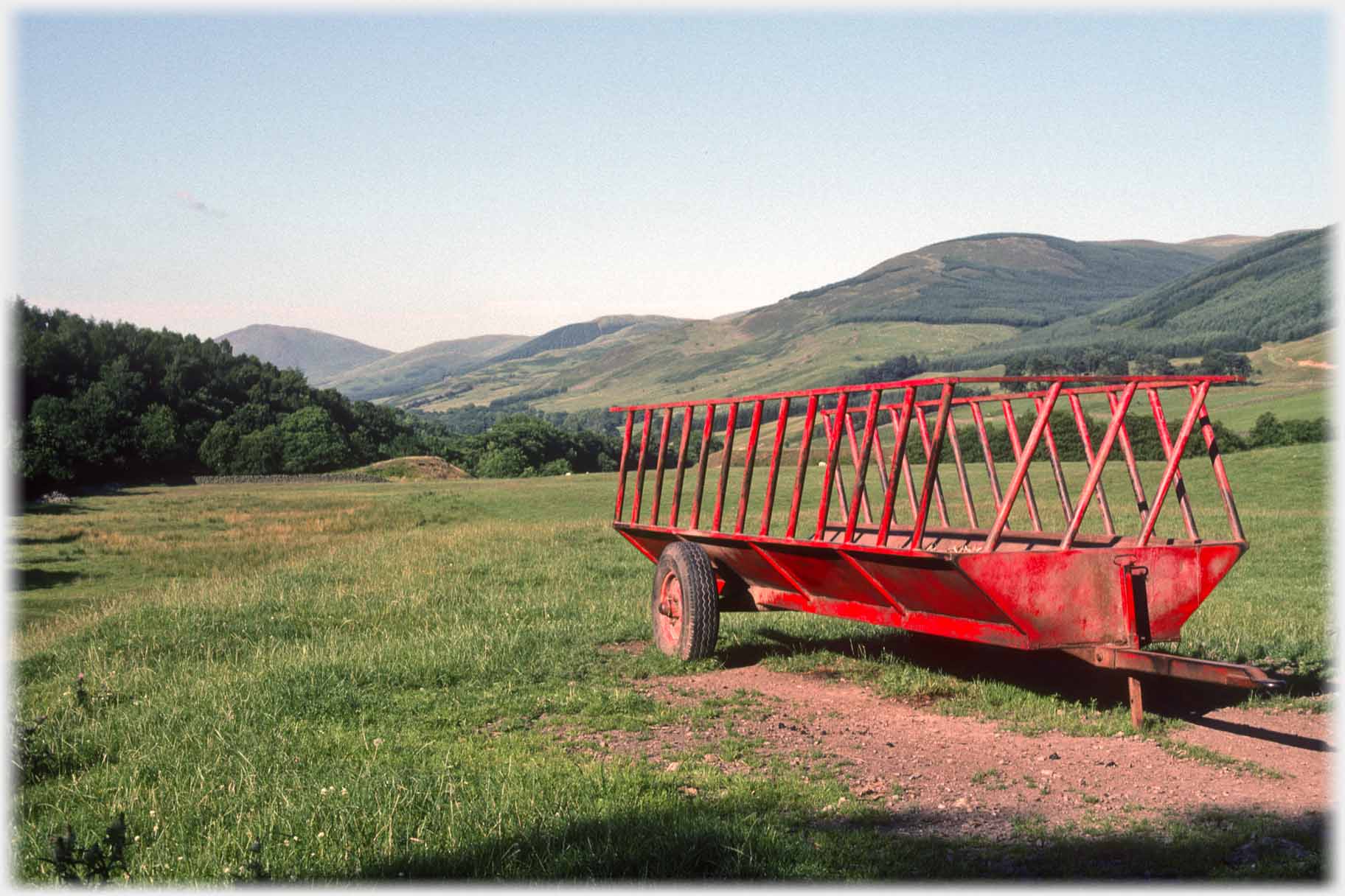 Red trailer in field, range of hills running away.