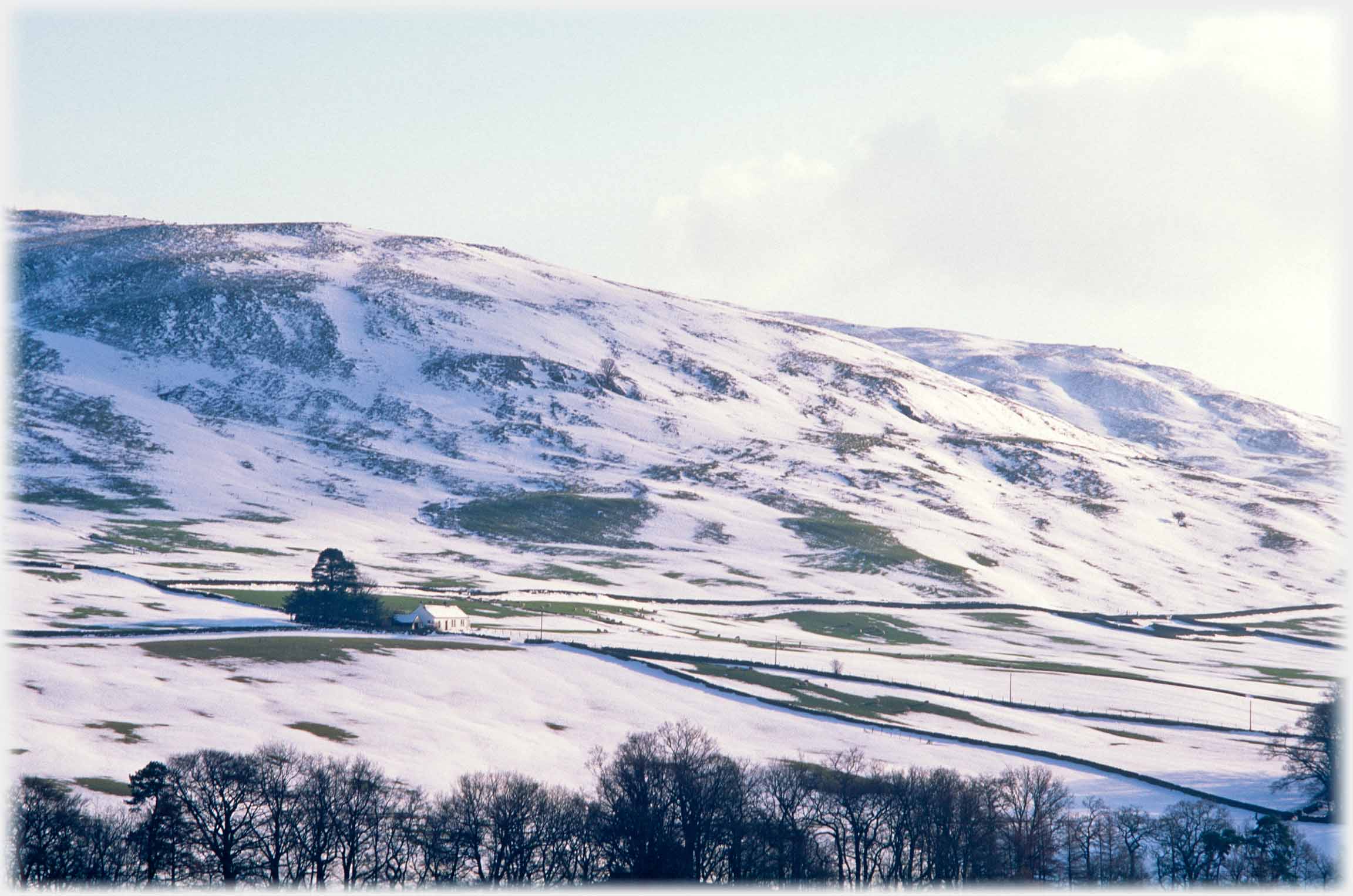 Snow covered hillside and fields with cottage at centre.