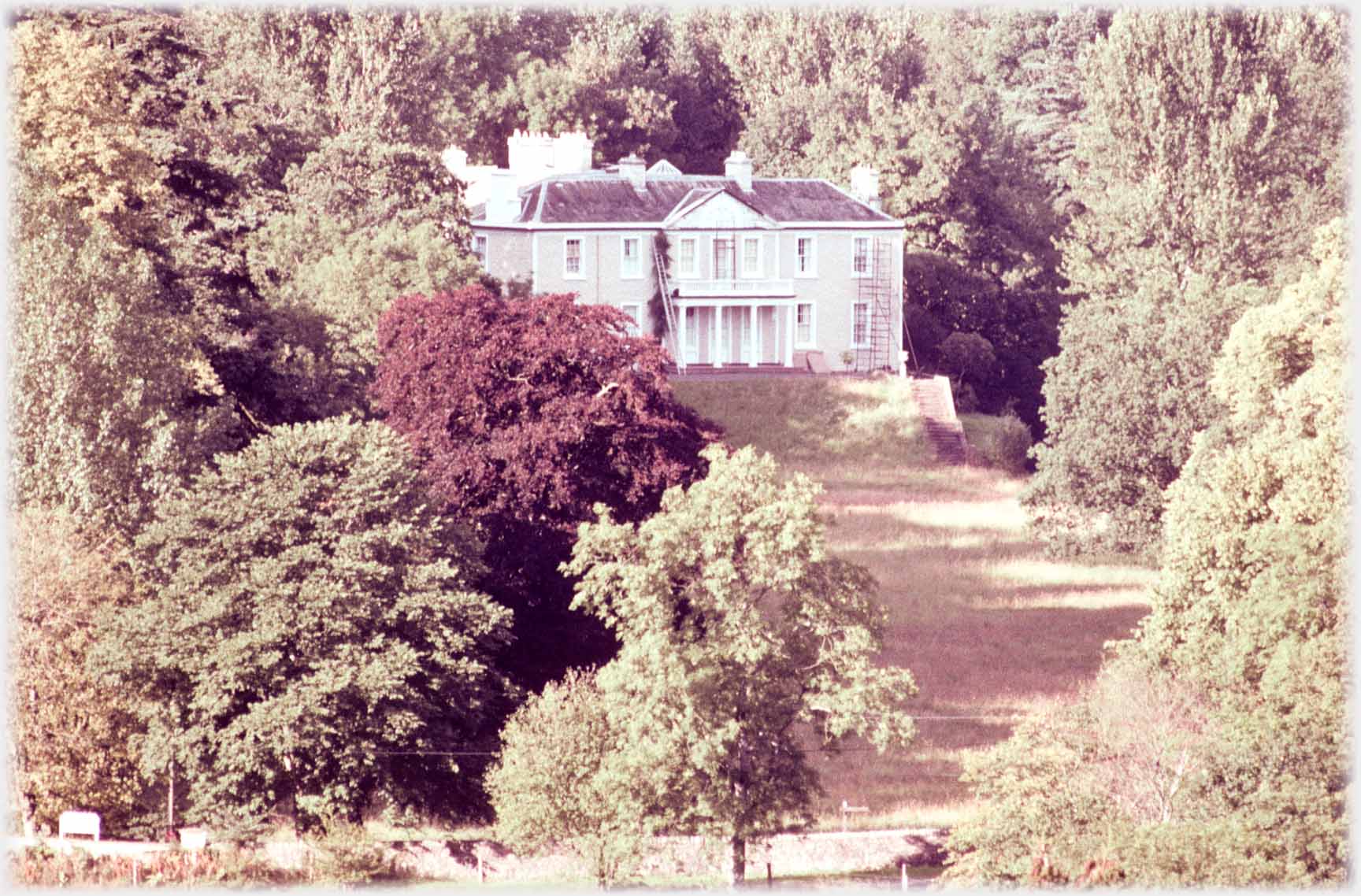 Mansion house with lawns and close set trees.