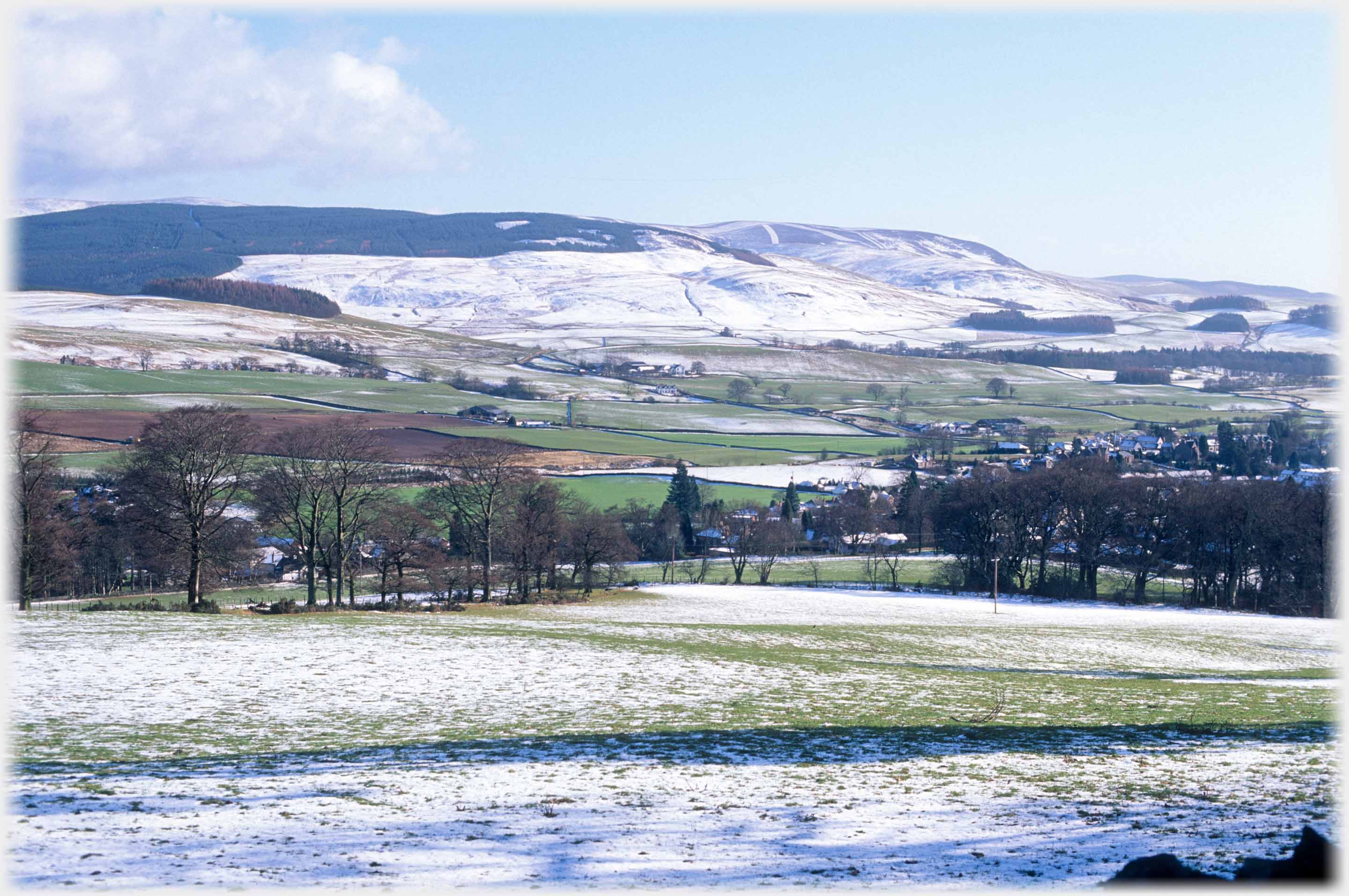 Lightly snow covered fields and hills with town buildings to the right.