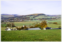 Trees on low hill seen across rooftops and fields.