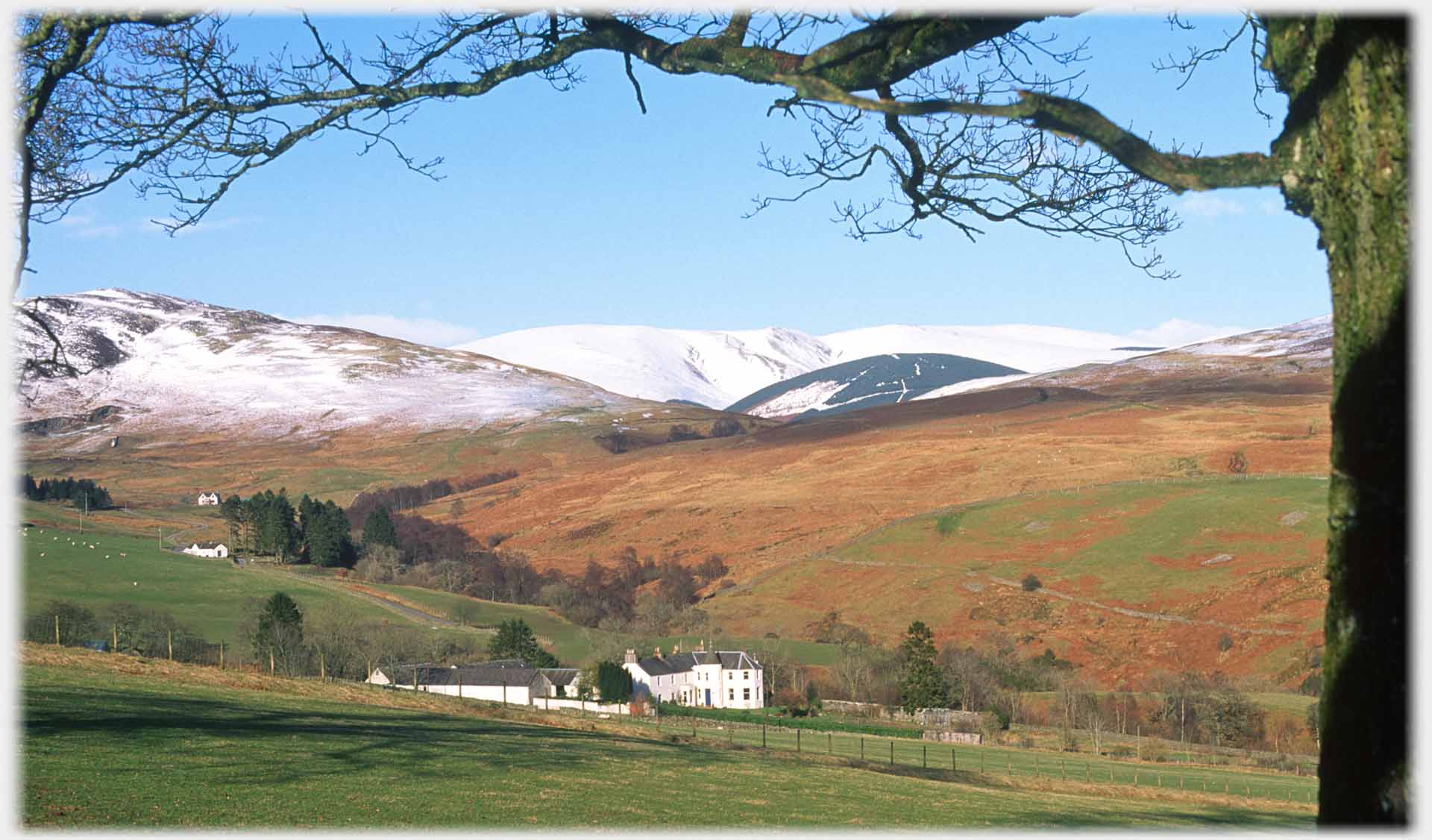 Large house in foreground, orange of bracken behind, high hills covered in snow.