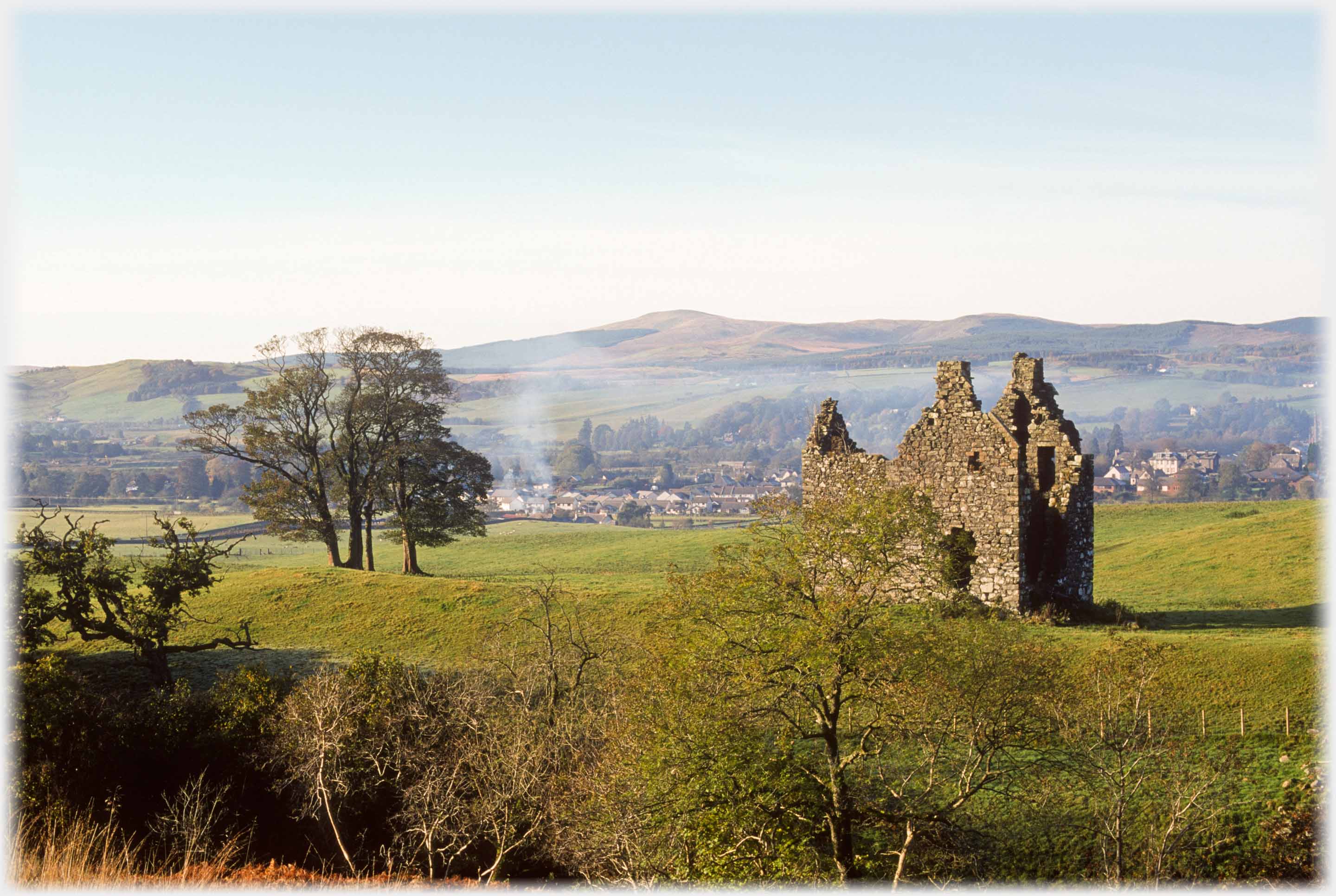 Ruined tower house, clump trees, town and hill beyond.
