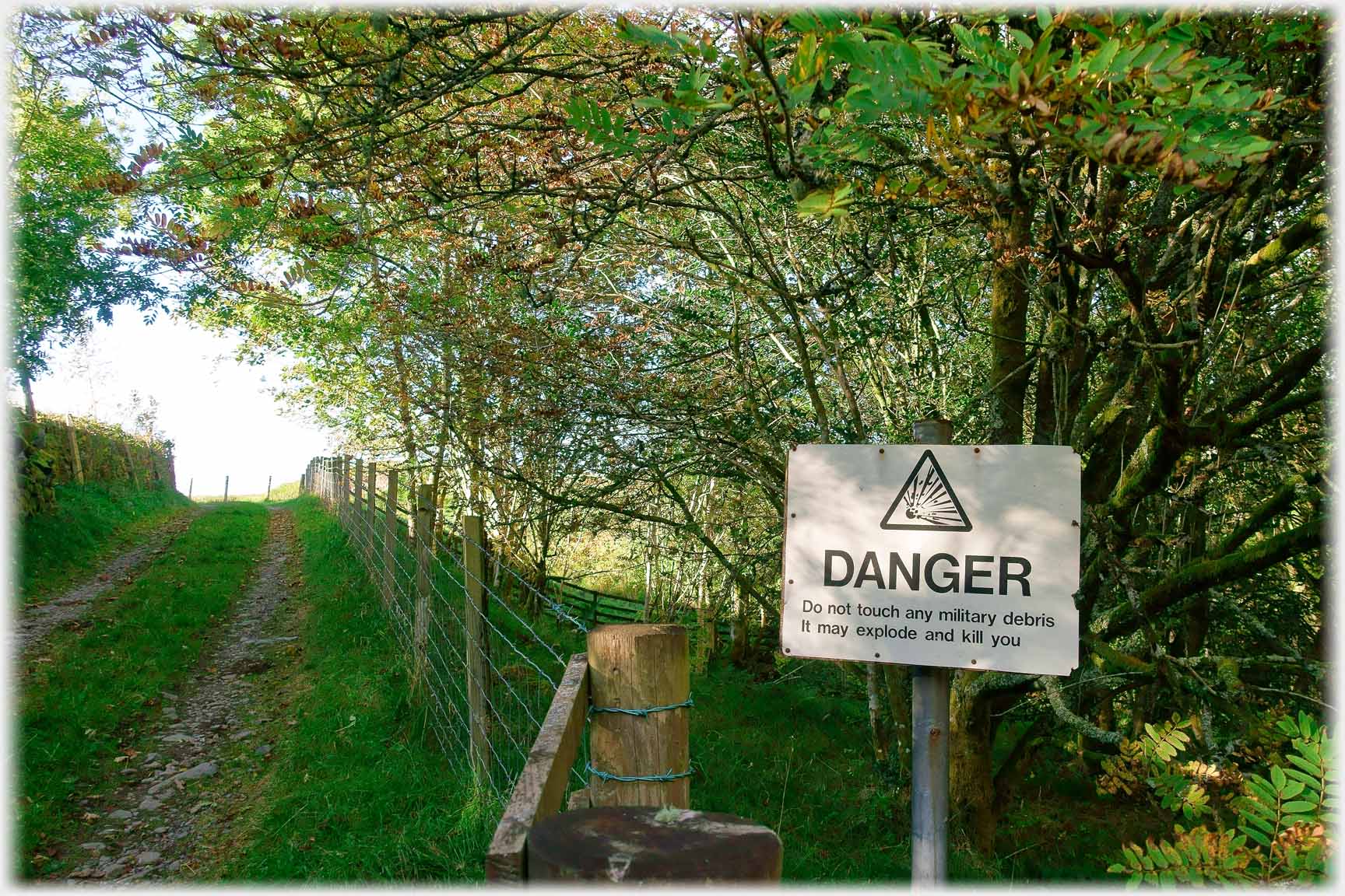 Old sign at lane side saying 'Danger, do not touch any military debris It may explode and kill you'.