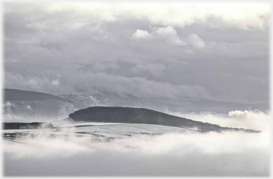 Black low hill standing out against white clouds and snow.