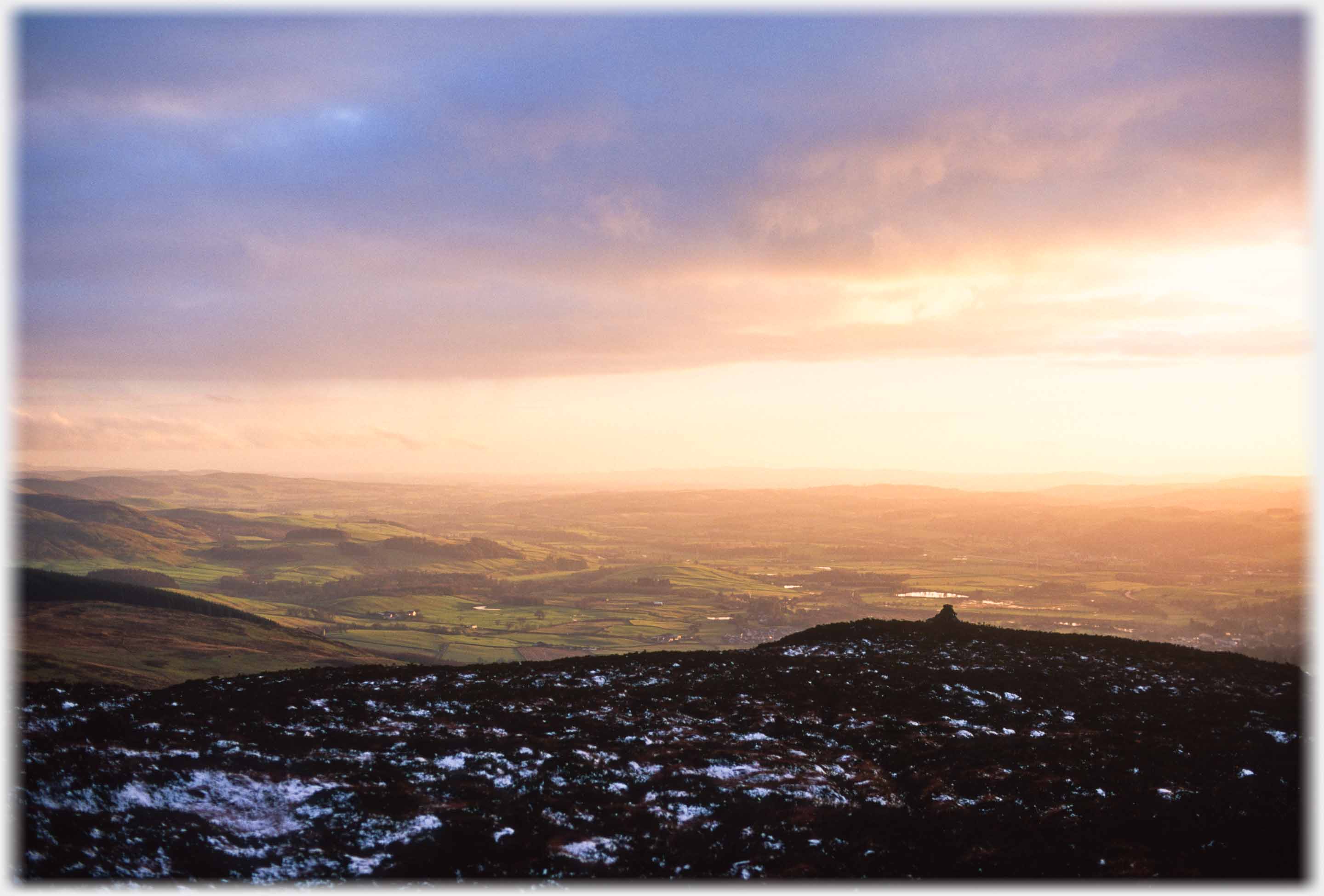 Firery sunset over plain, snow speckled hilltop with triangulation point in foreground.