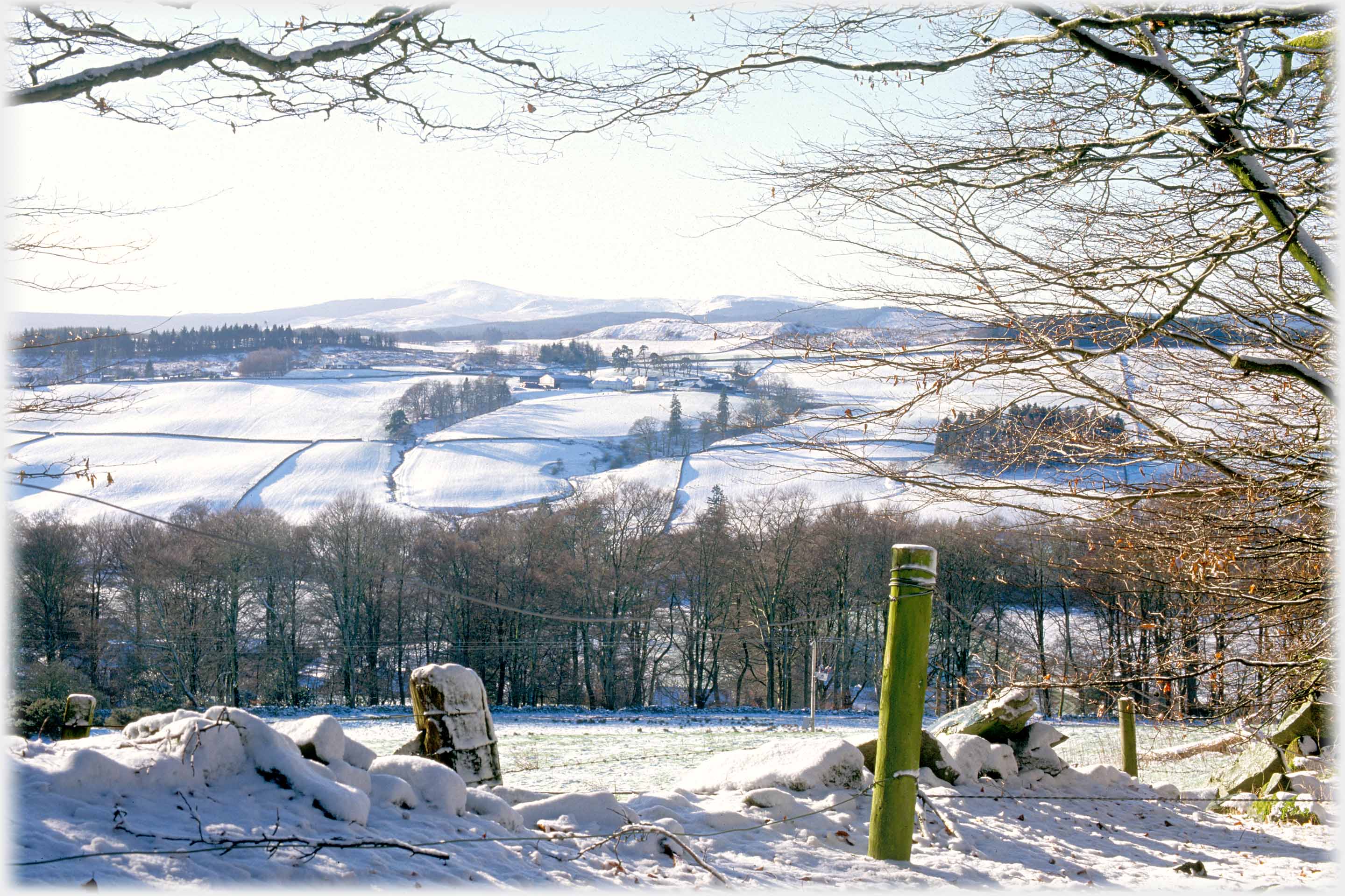Snow covered landscape with posts and broken dyke in foreground, distant peaked hill.