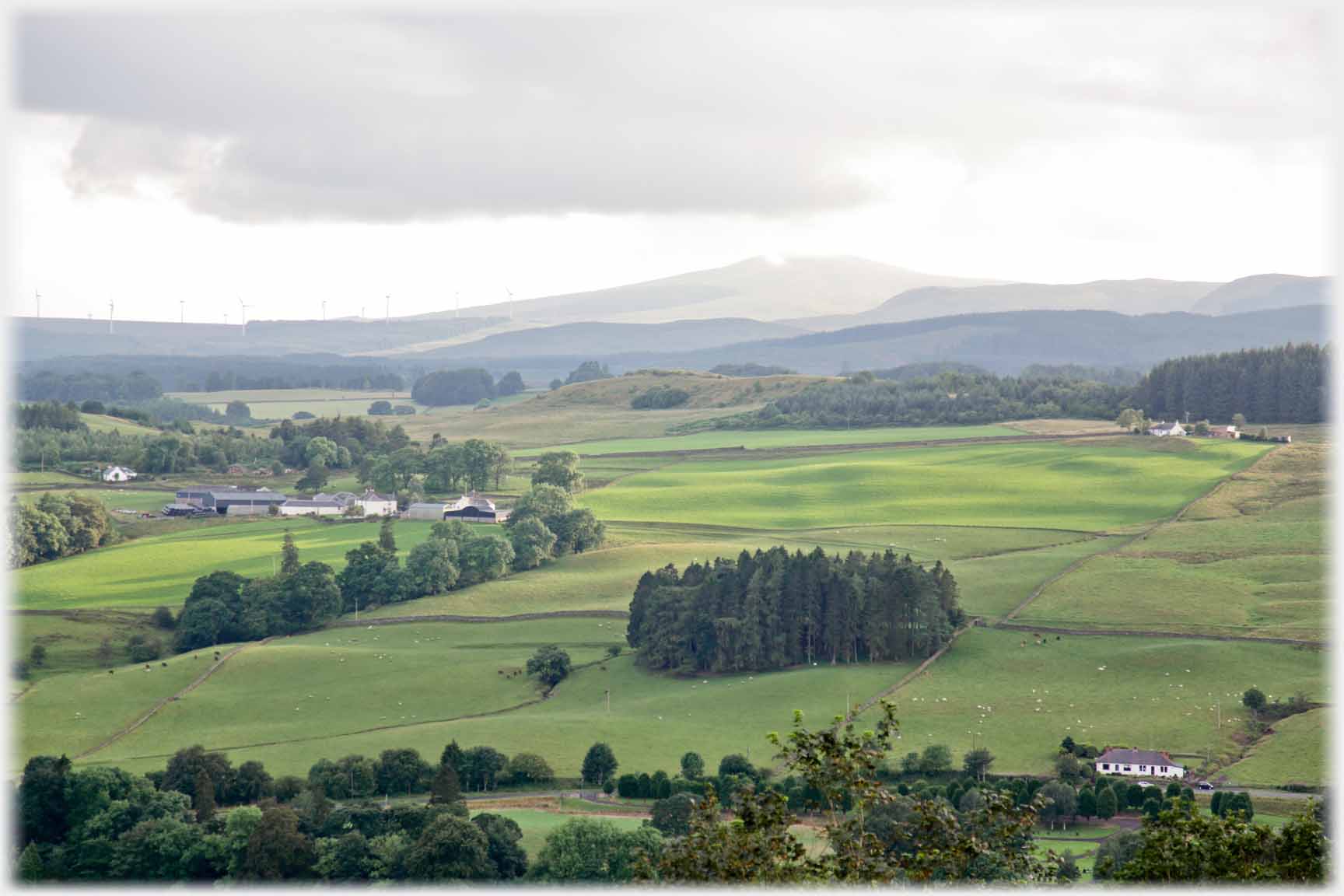 Similar view of farm and hillside with distant hill having mist just touching it.