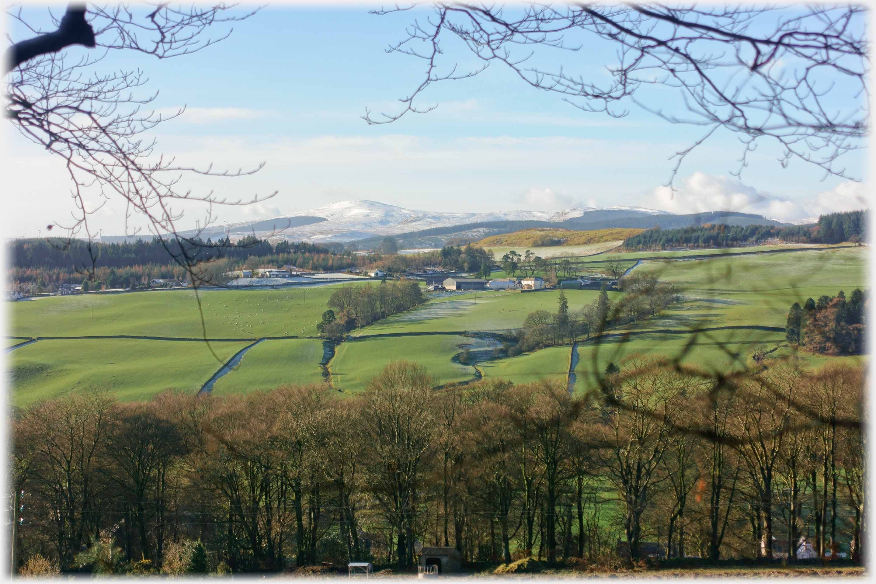 Hillside and farm clear of snow, but frost in shadow of trees, and distant hill snow covered.