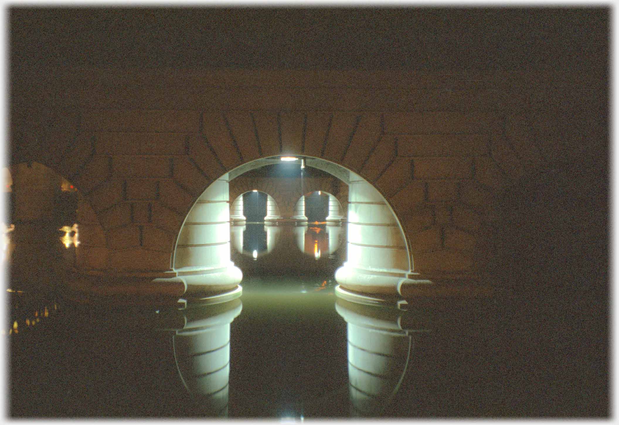 View through arches supported by large stone pillars in river.