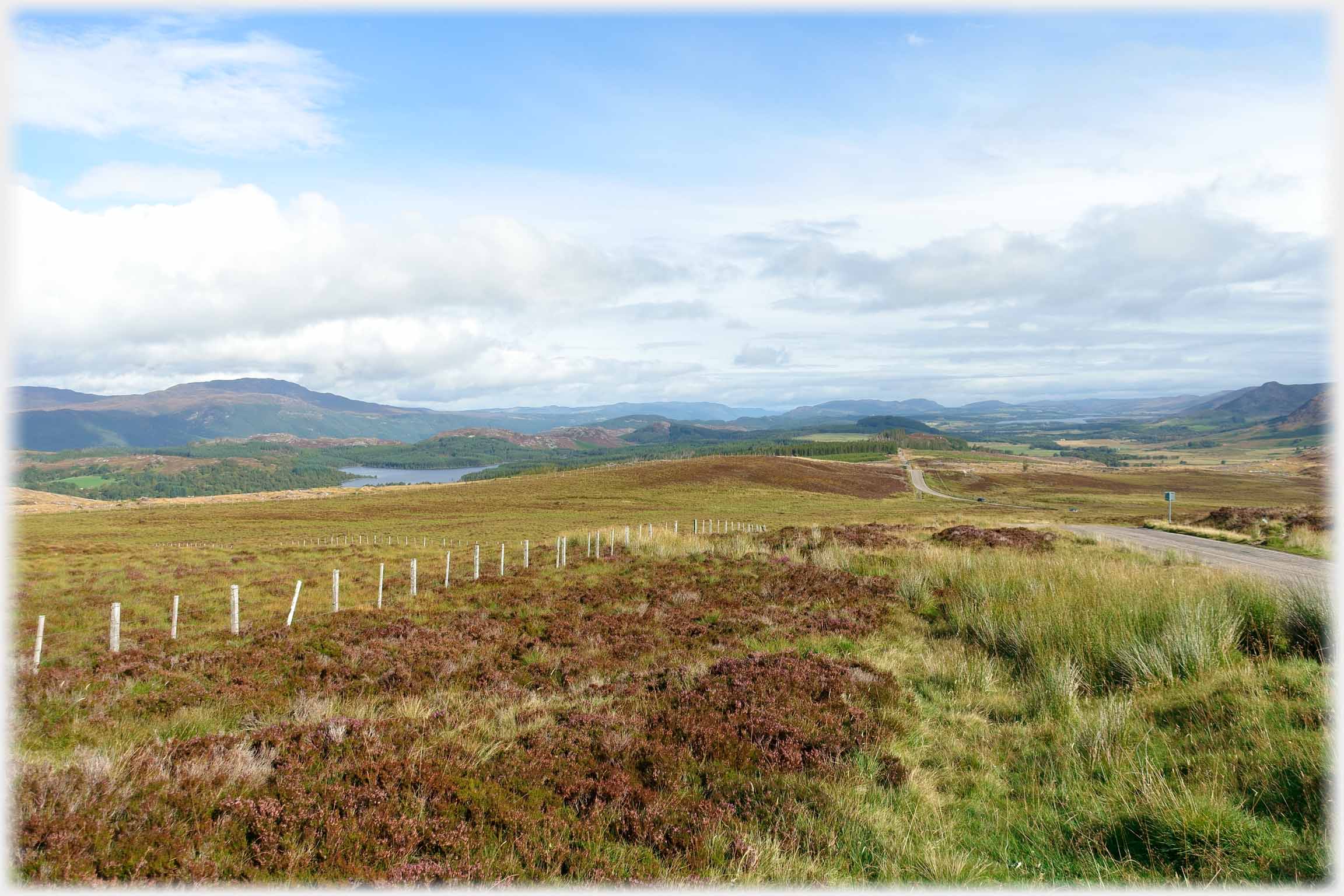 Moorland with small road decending away into distance and low hills.