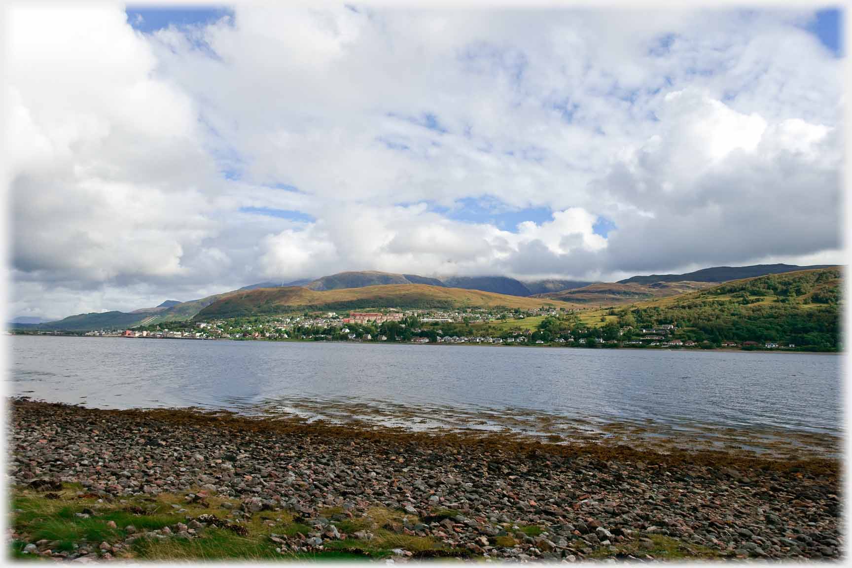 Looking across loch to distant town spreading across hillside down to water.
