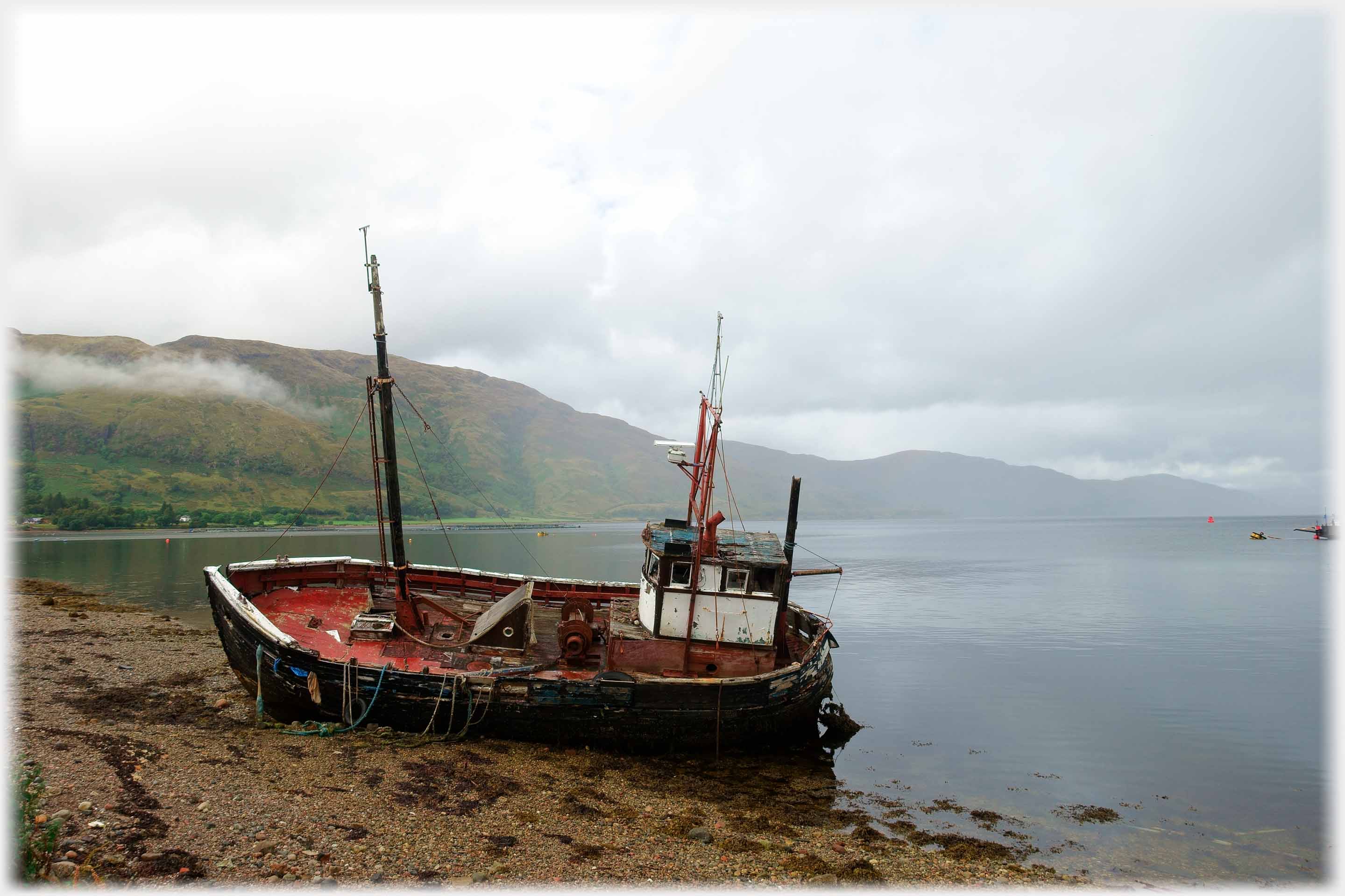 Old fishing boat still with marsts and cabin beached at water's edge.