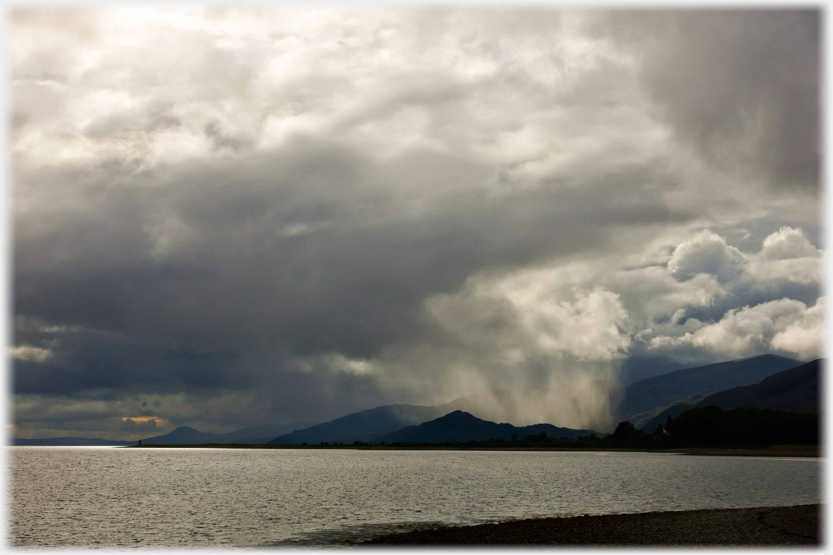 Clouds letting down shower across loch and behind silouhetted hill.