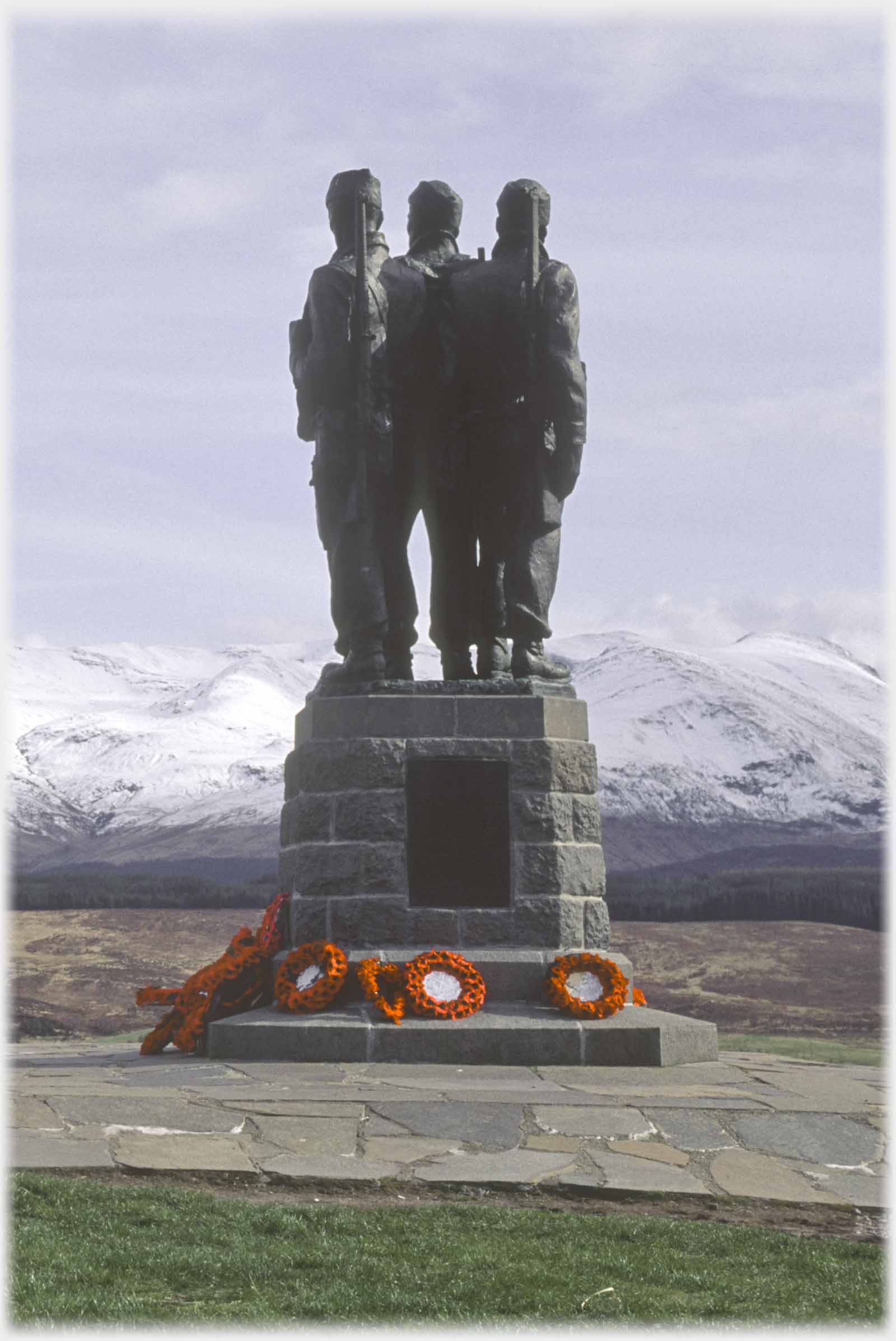 Three soldiers on plinth, poppy wreaths below.