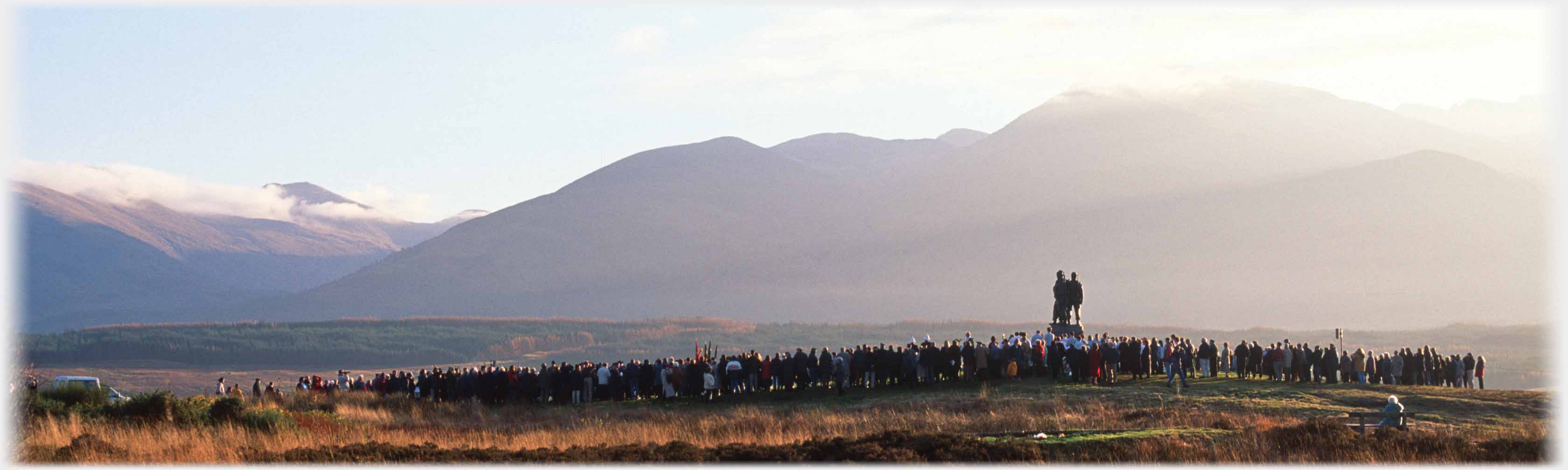 Monument against background of hills with crowd of several hundred along line of picture.